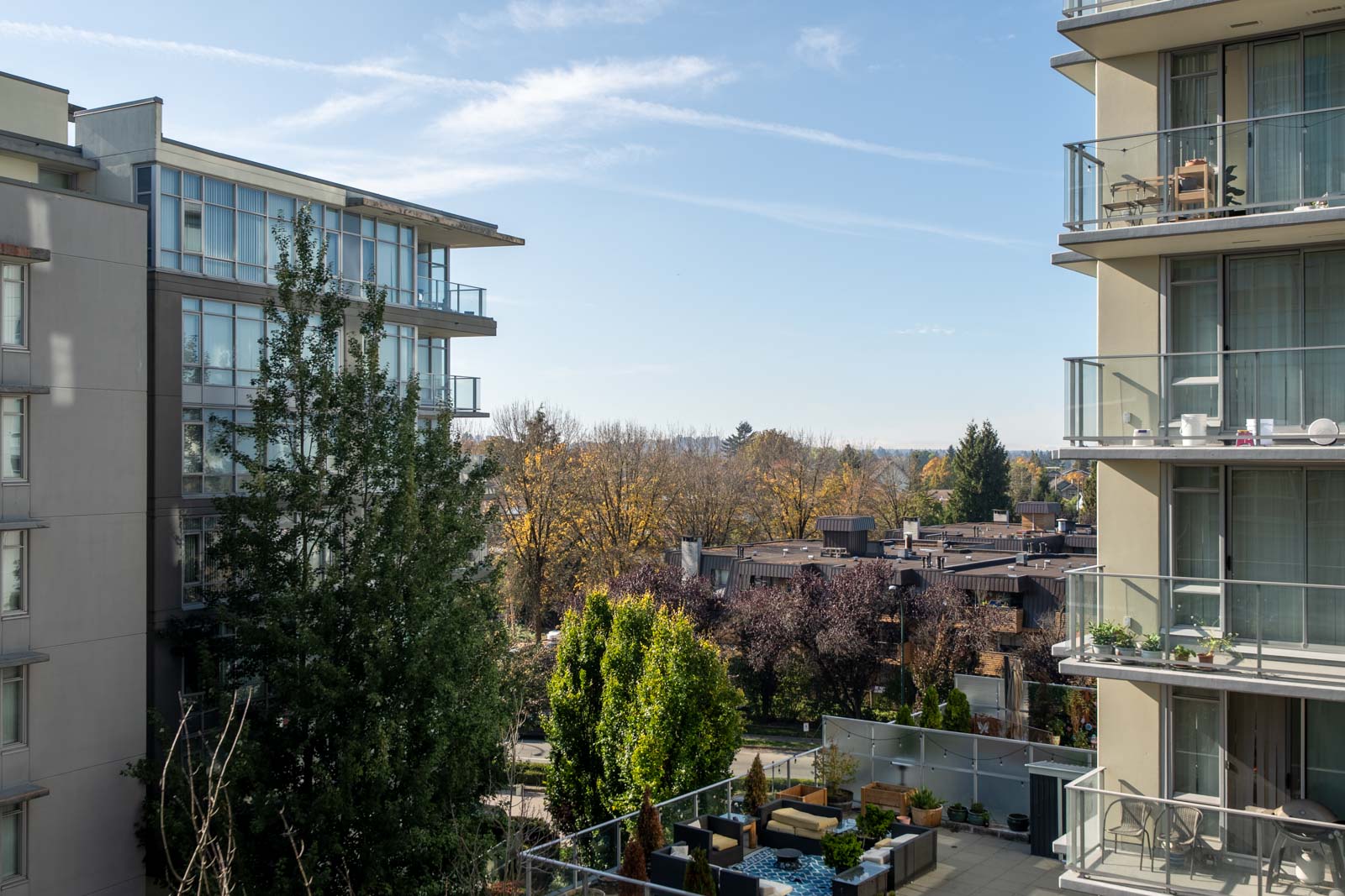 View between two Vancouver condo buildings at 4818 Eldorado Mews, showing trees and a rooftop patio with seating.