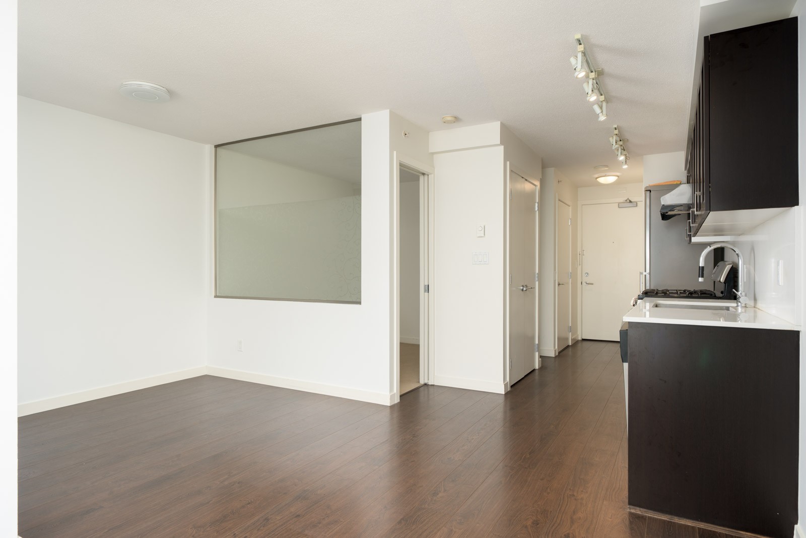 Open-concept interior at 4818 Eldorado Mews with dark wood floors, a glass-panel wall, and a dark-cabinetry kitchen.