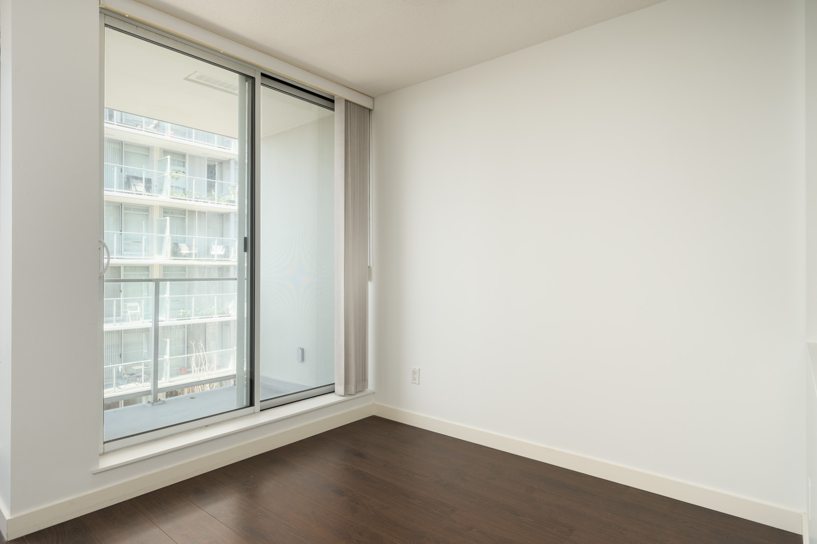 Empty room at 4818 Eldorado Mews with dark wood floors, white walls, and a glass sliding door to a balcony.