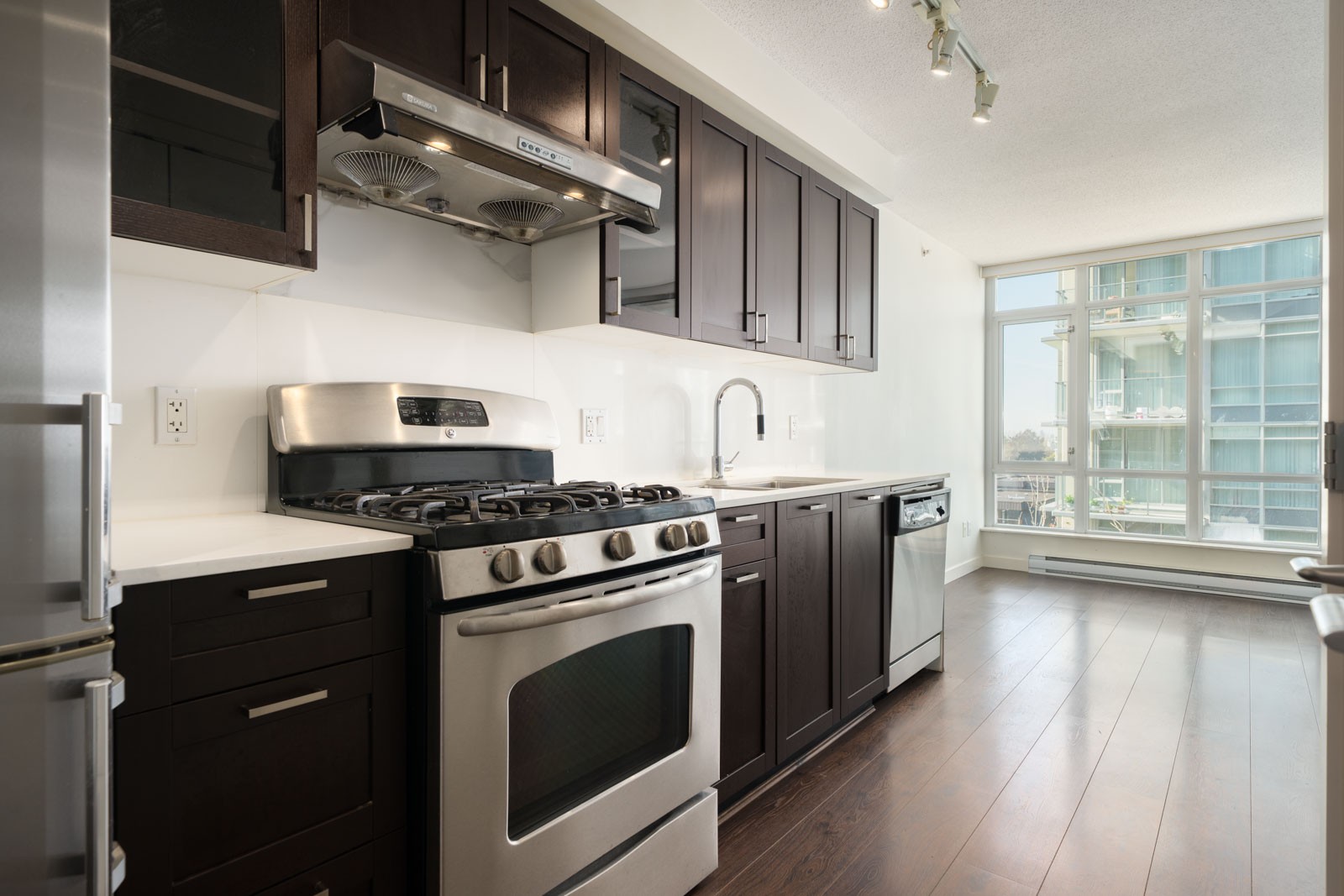 Kitchen at 4818 Eldorado Mews with dark wood cabinets, stainless gas stove, and windows overlooking Vancouver condos.