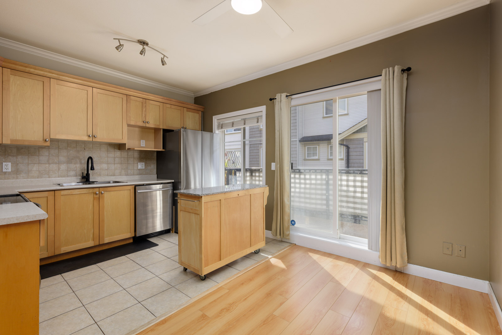 Kitchen with light wood cabinets, stainless steel appliances, a mobile island, and sliding door in a Surrey townhouse.