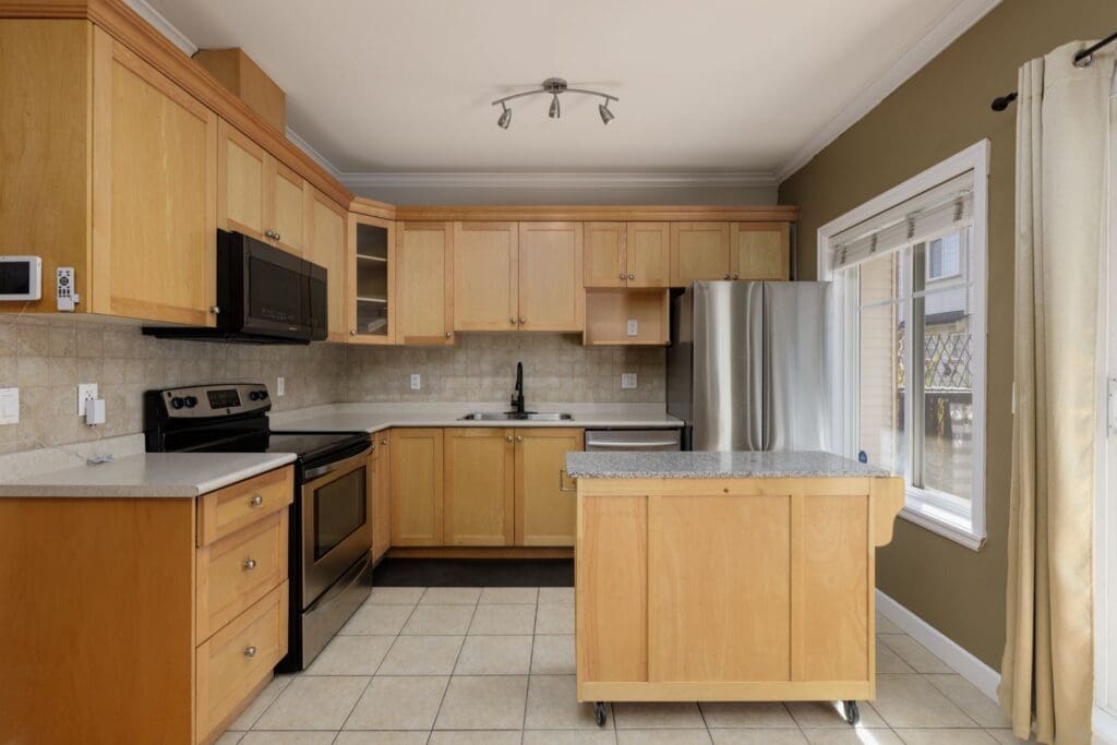 Modern kitchen in a Surrey townhouse with light wood cabinets, stainless steel appliances, a stone island, and tile floors.