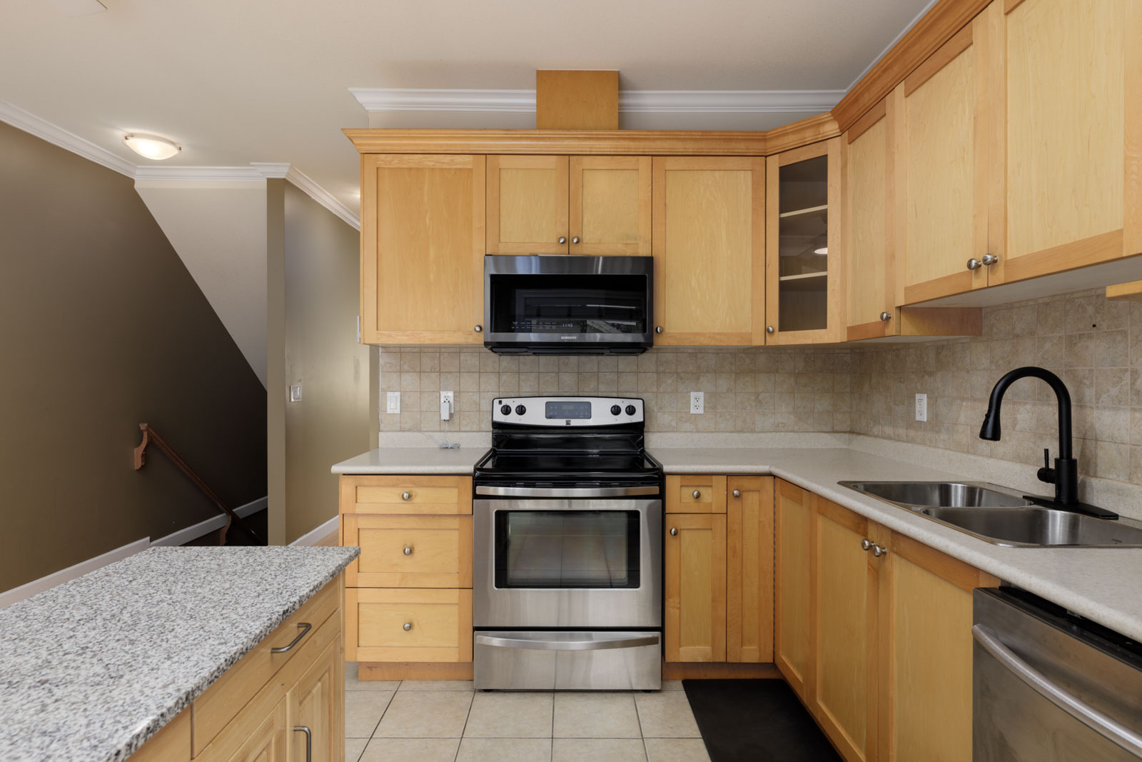 Kitchen in a Surrey townhouse featuring light wood cabinets, stainless steel appliances, and a granite island.