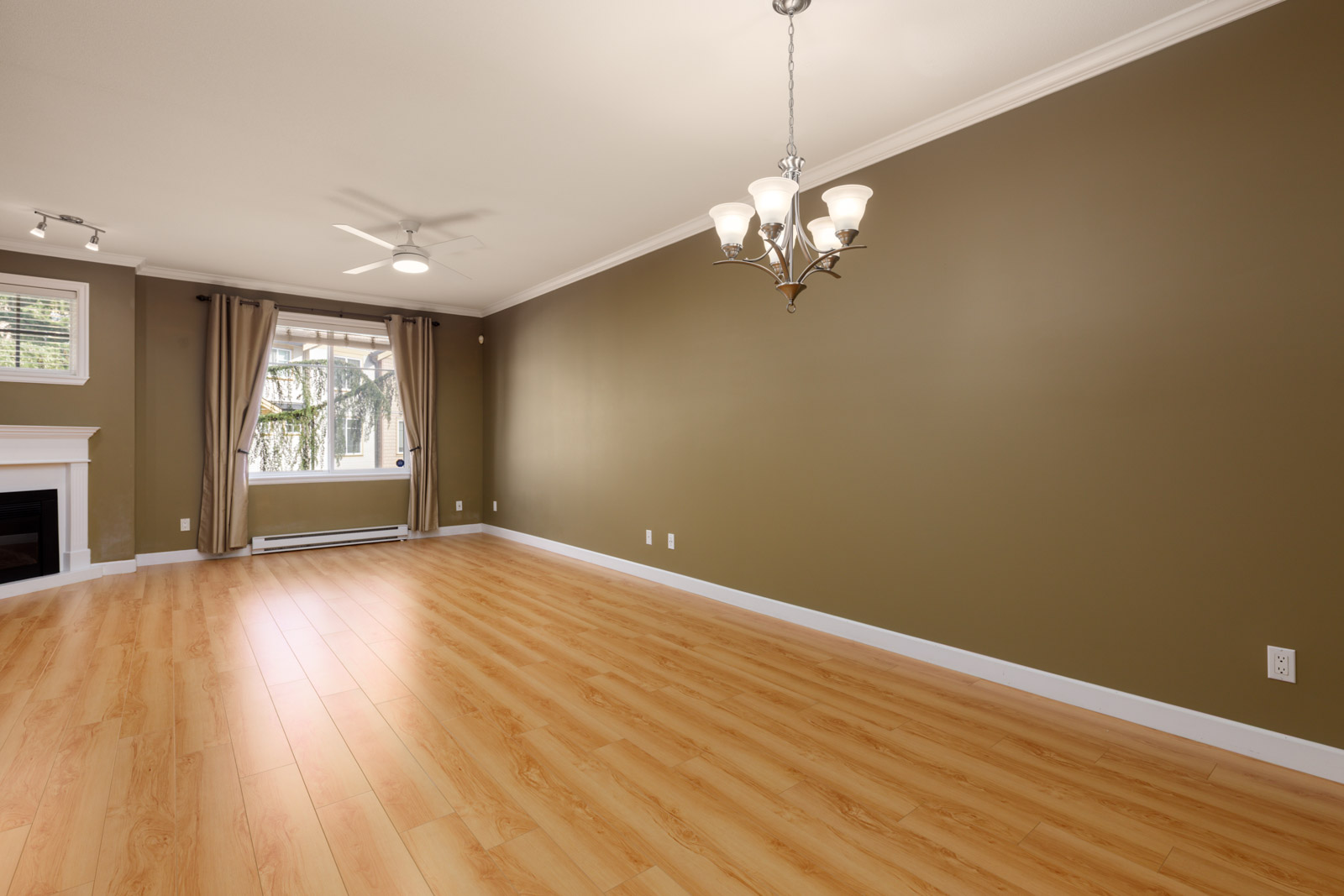Empty Surrey townhouse room with light wood floors, dark olive-green walls, a fireplace, and a chandelier.