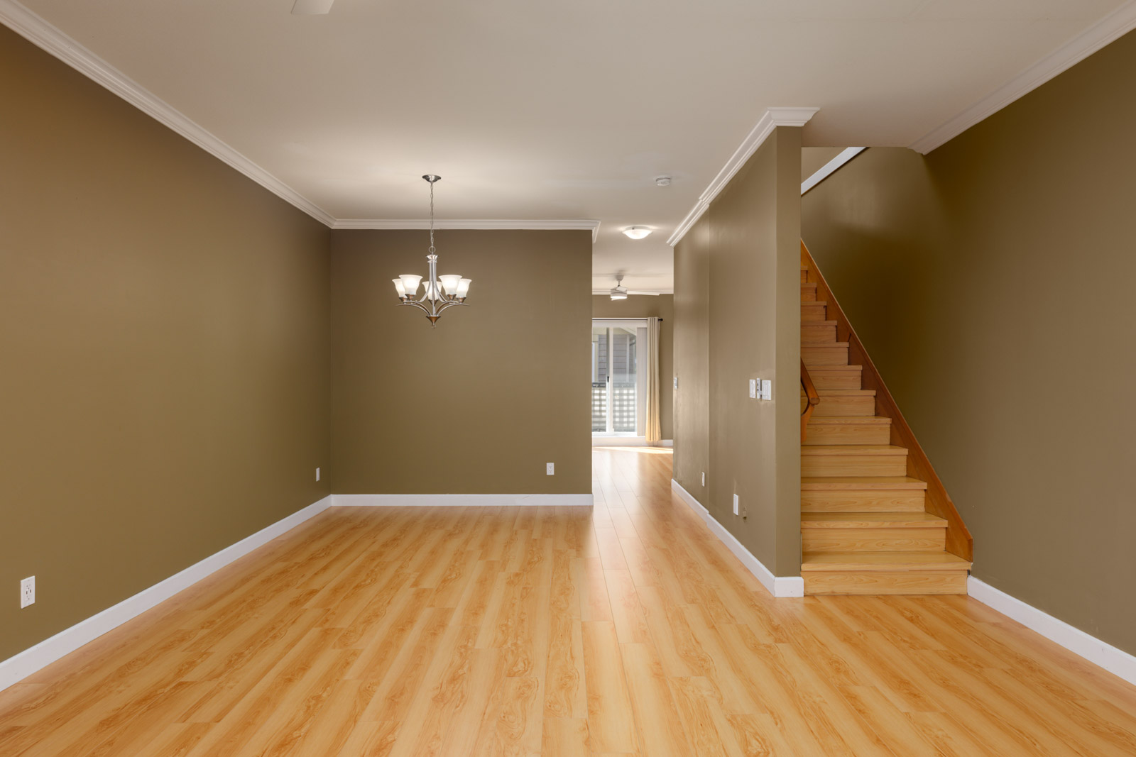 Empty Surrey townhouse living room with brown walls, wood flooring, a chandelier, and a staircase.