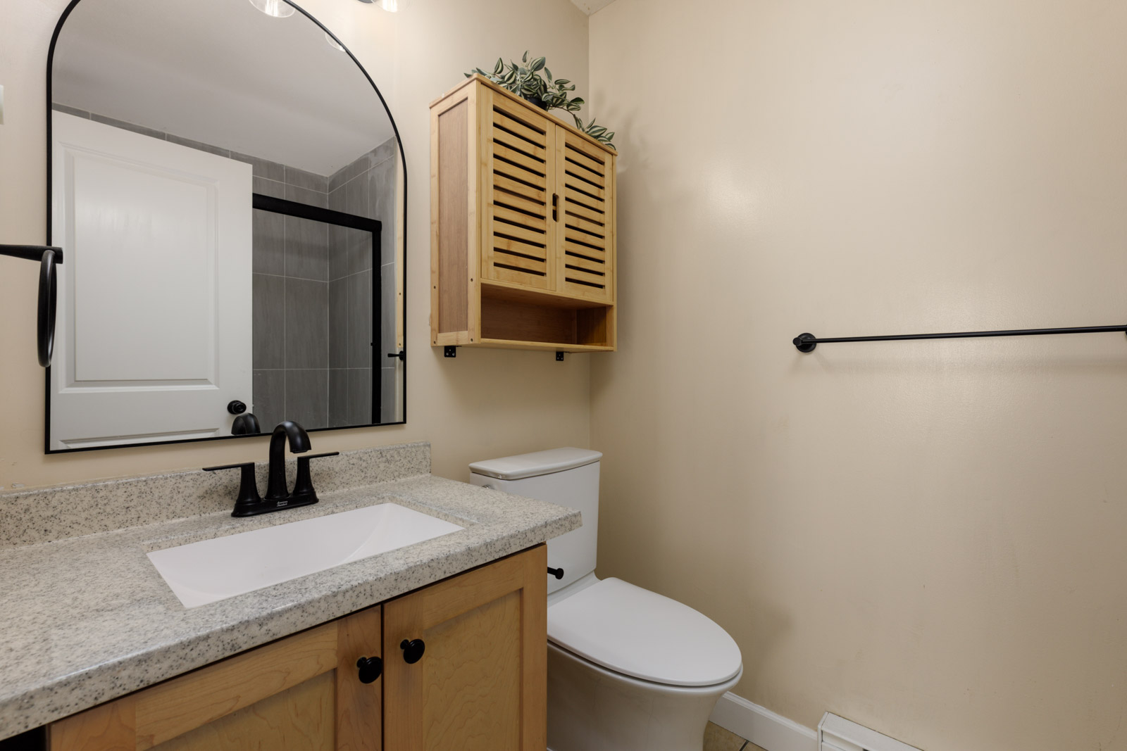 Bathroom vanity with a light stone countertop, arched mirror, toilet, and wooden wall cabinet at 8633 159 St, Surrey.