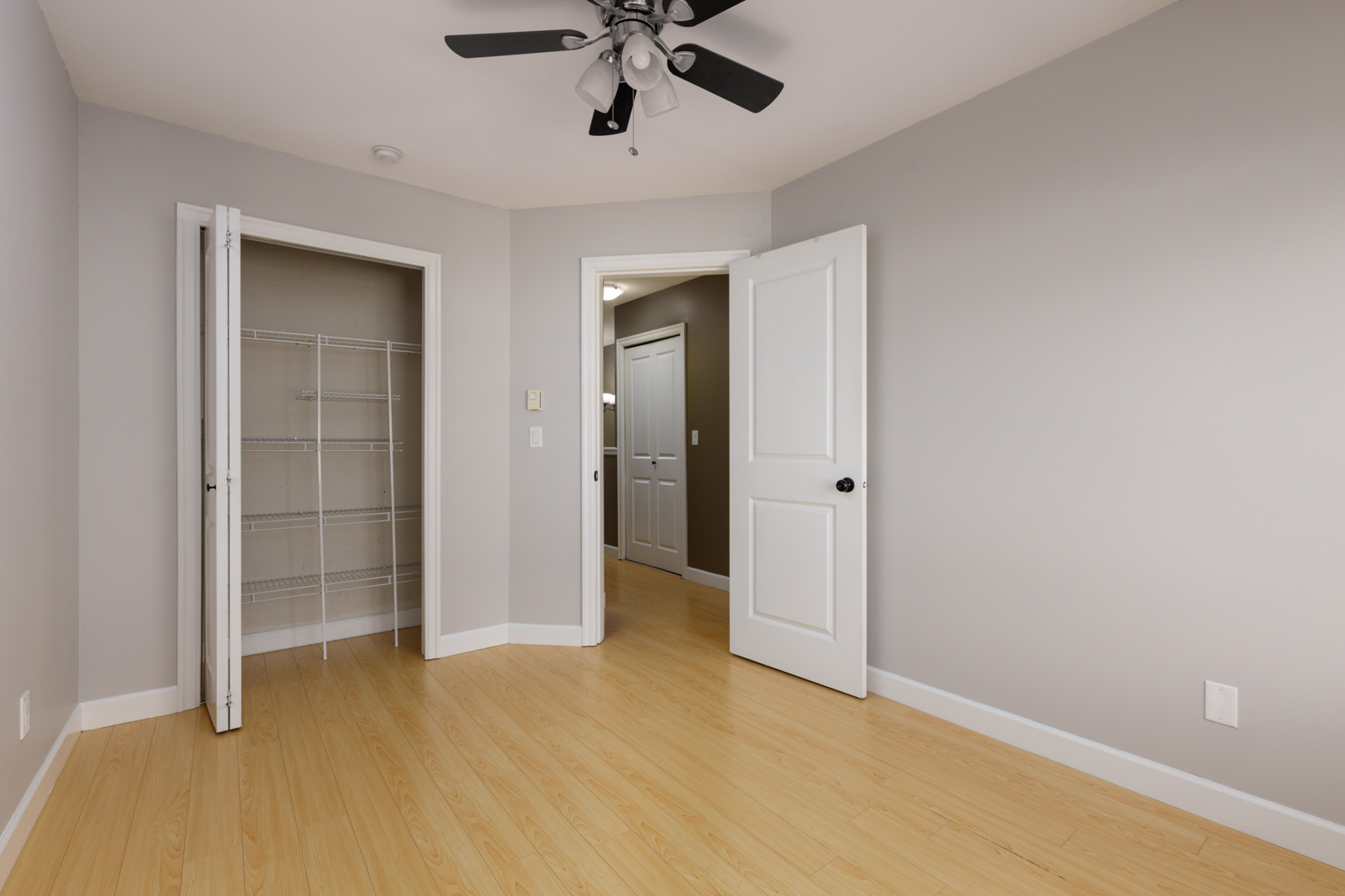 Empty Surrey townhouse room with light wood floors, an open wire-shelved closet, and a doorway to the hallway.