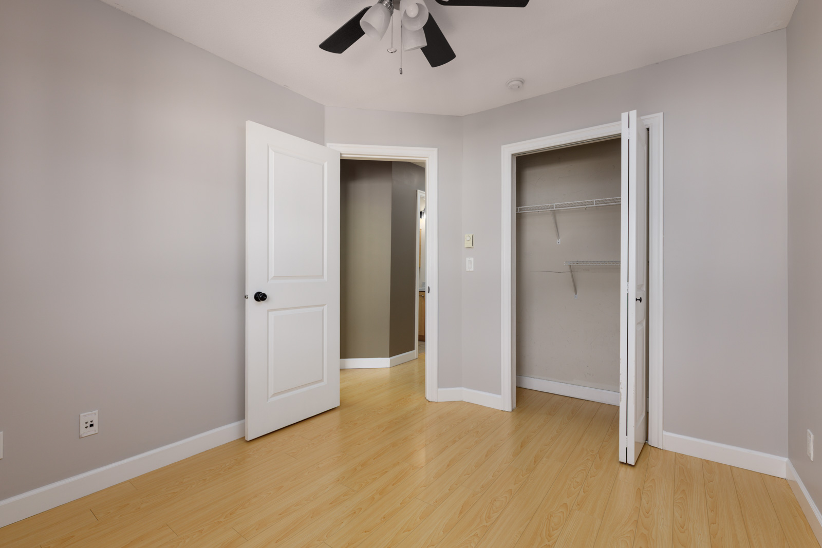 Empty Surrey townhouse room with light wood floors, a ceiling fan, hallway doorway, and closet with wire shelving.