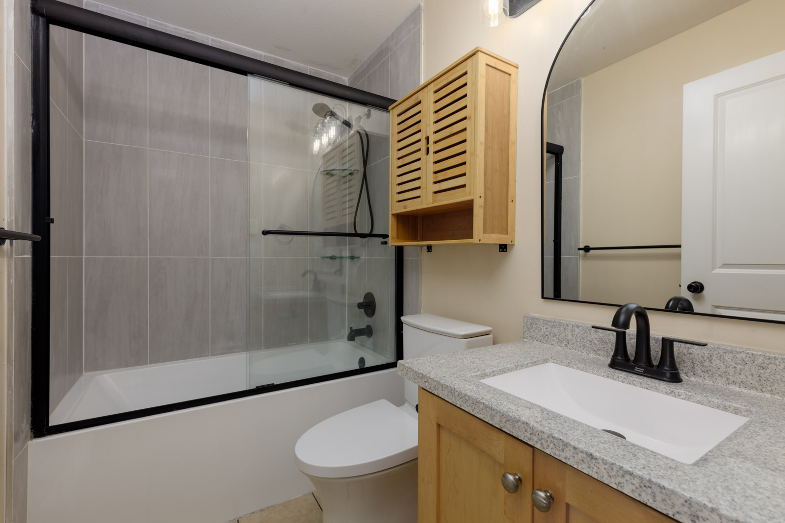 Bathroom in a Surrey townhouse with a bathtub-shower combo, wooden cabinet, toilet, and vanity with a stone countertop.