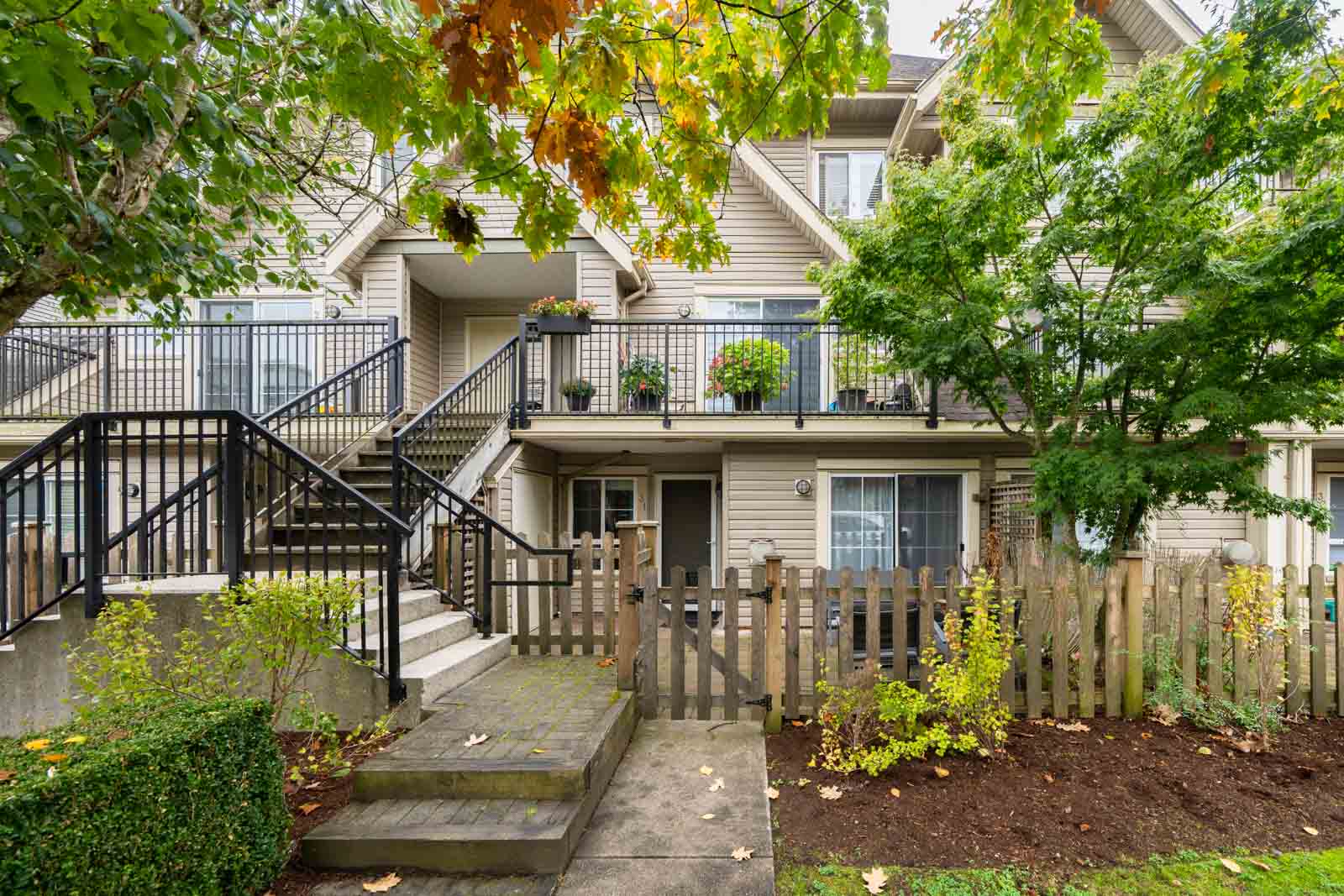 Multi-level townhouse at 9339 Alberta Rd featuring beige siding, a wooden-fenced front patio, and an outdoor staircase.