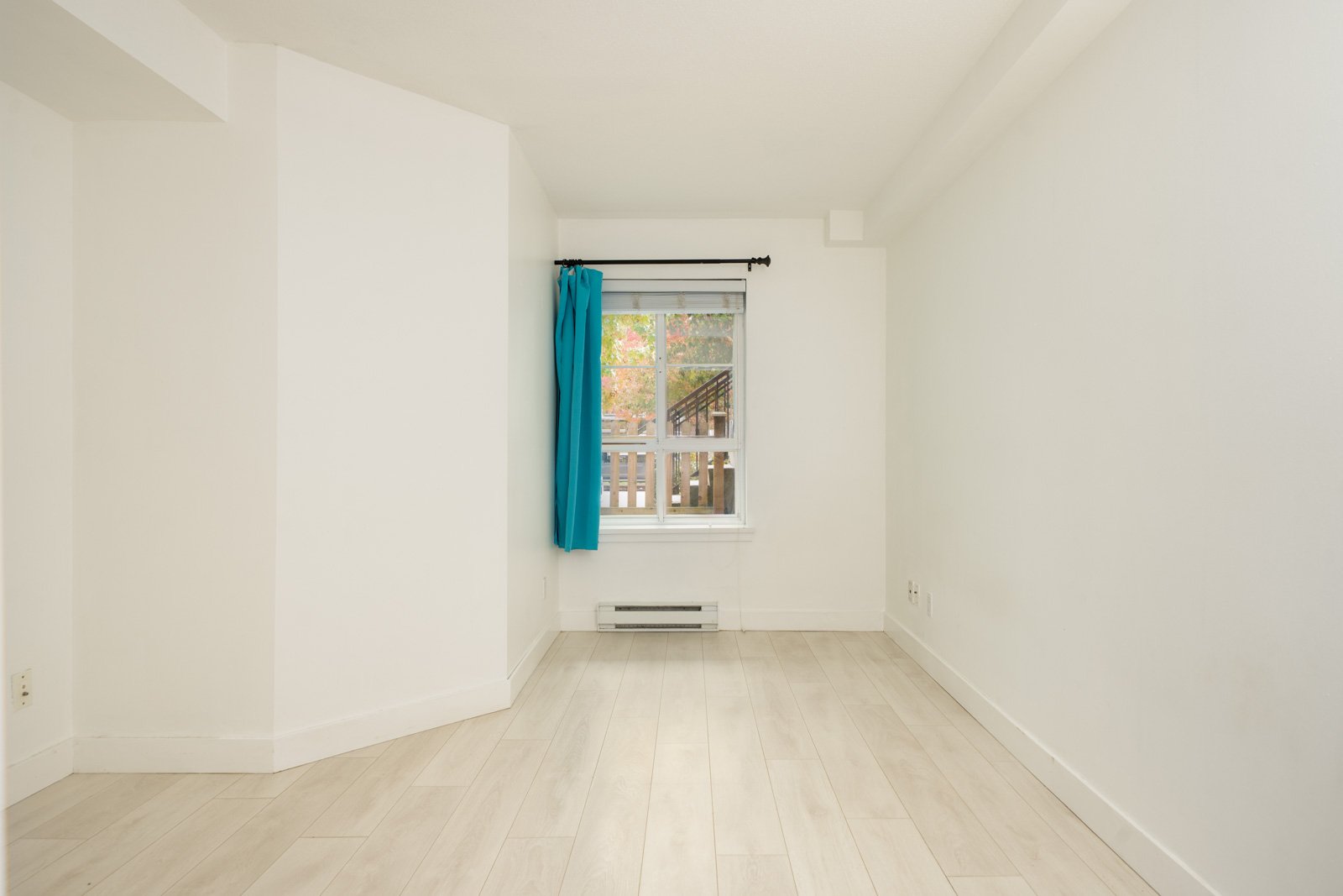 Empty room with white walls, light wood floors, and a blue-curtained window viewing a deck at 9339 Alberta Rd, Richmond.
