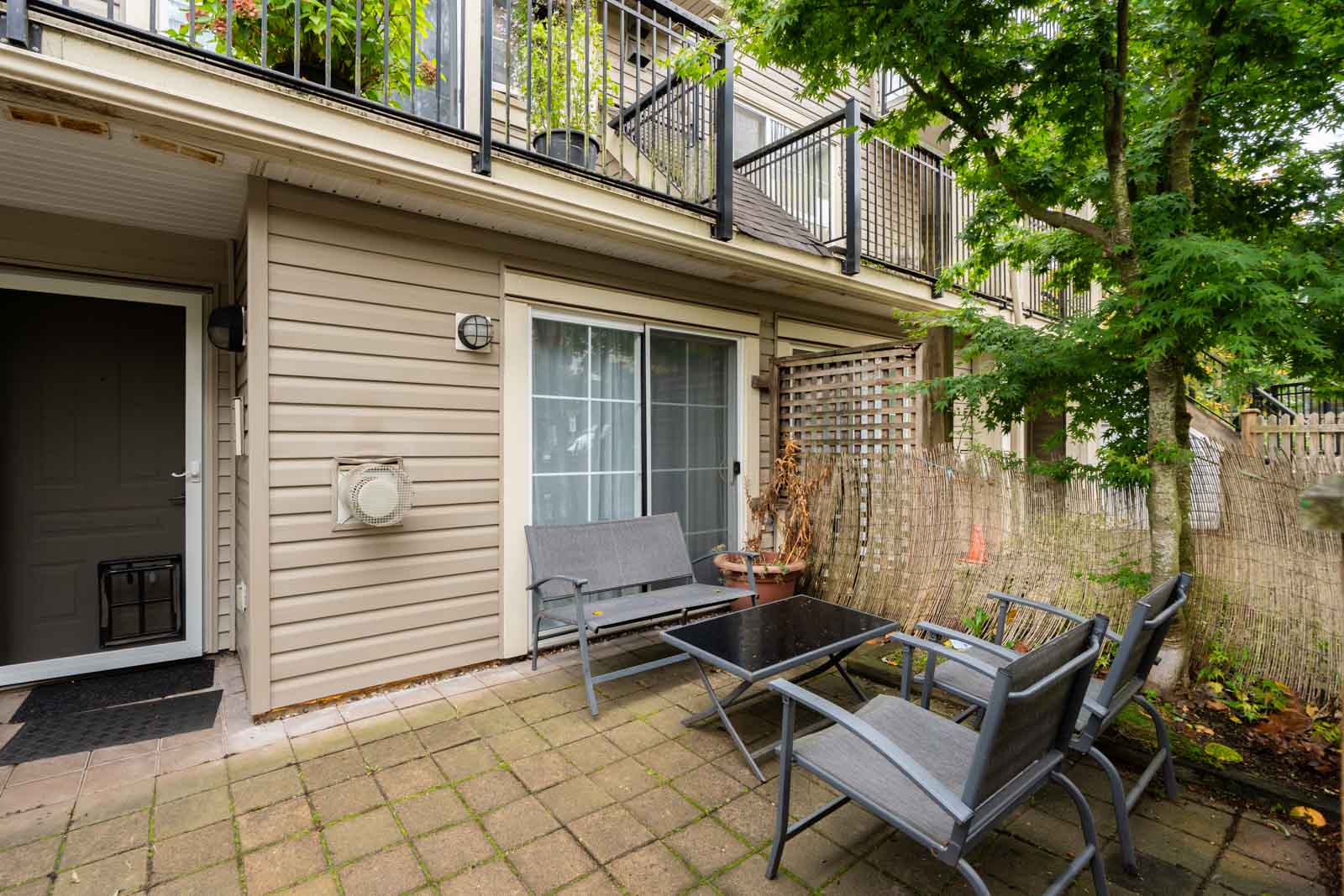 A small paved patio with a metal table and three chairs at a 9339 Alberta Rd townhouse, featuring a sliding glass door.