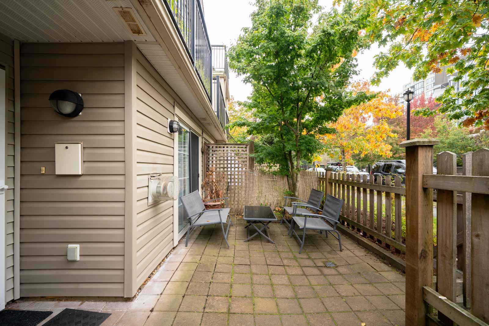 Three gray chairs and a small table on a patio at a Richmond townhouse with tan siding.