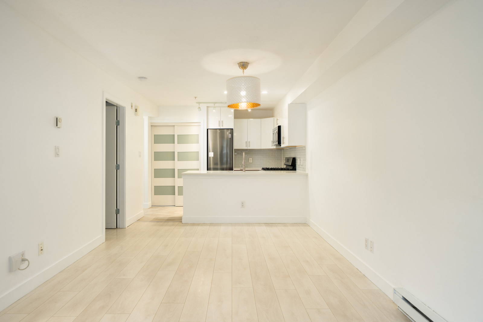 Open-concept Richmond townhouse living area with light wood-style flooring and a small kitchen with white cabinetry.