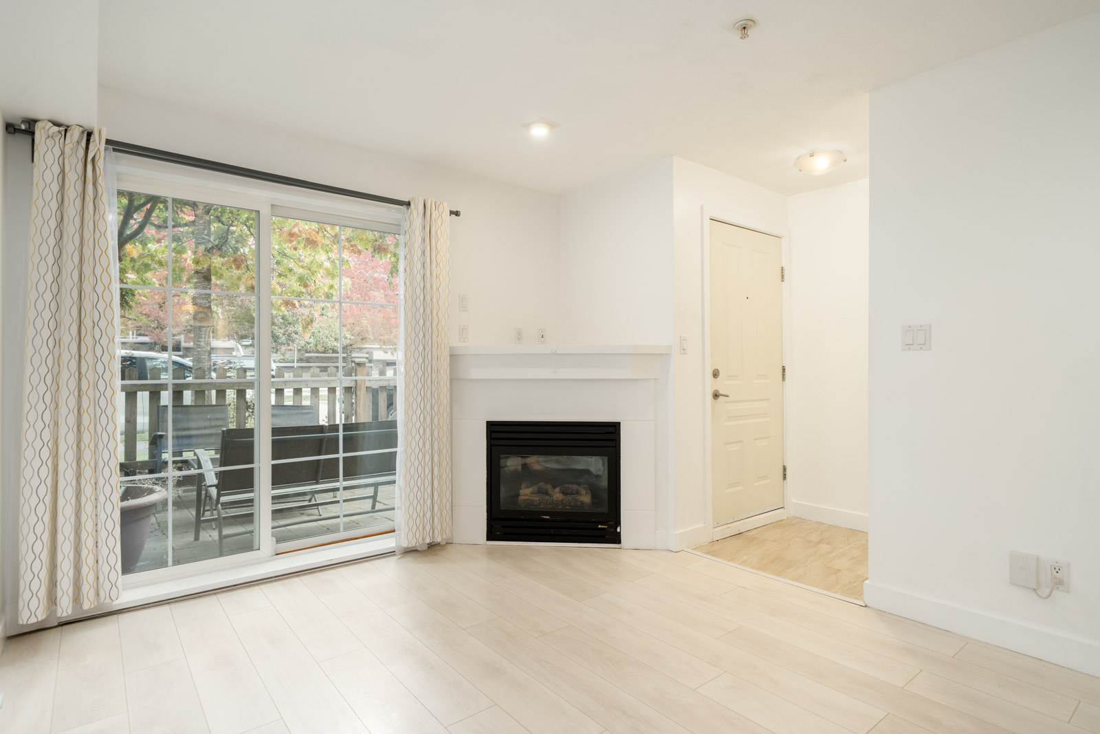 Empty living room in a Richmond townhouse with wood-look floors, a corner fireplace, and a patio sliding glass door.