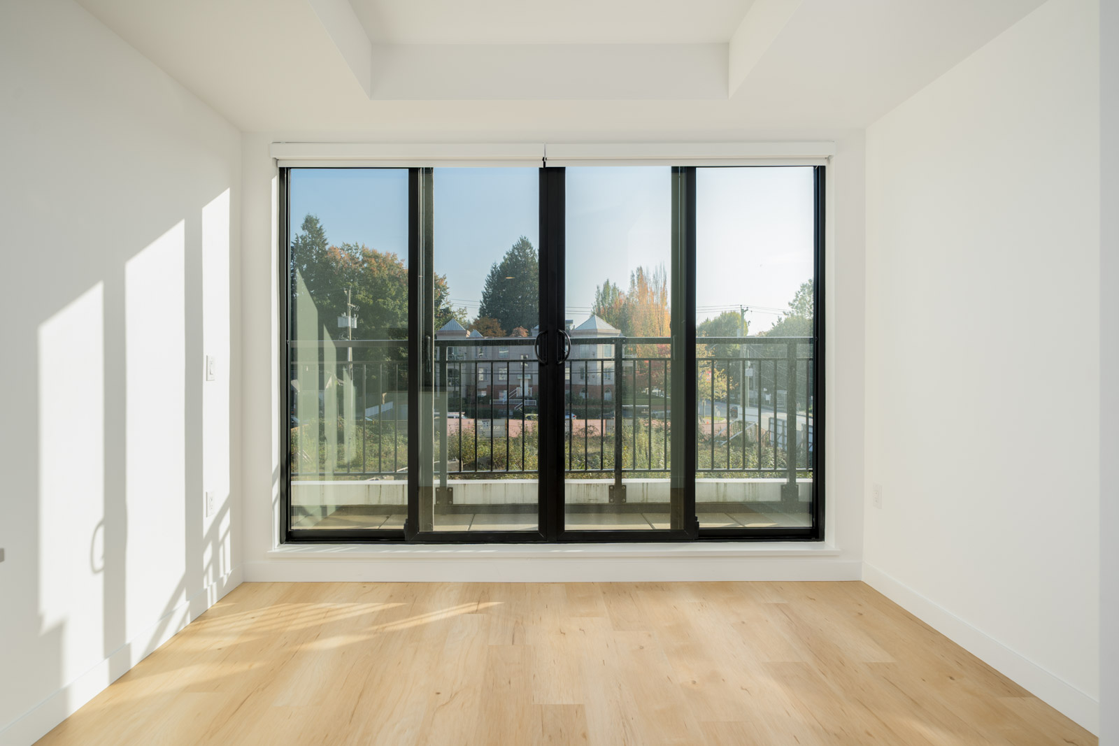 Empty 2nd-floor office on Shaughnessy St with light wood floors and a black-framed sliding glass door to a balcony.