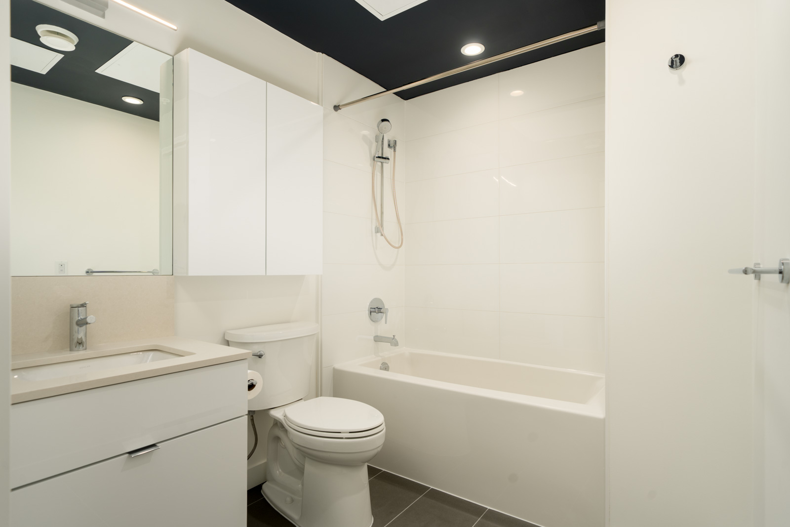 Bathroom at 2446 Shaughnessy St with a white vanity, toilet, and a bathtub with a shower head against white tiled walls.