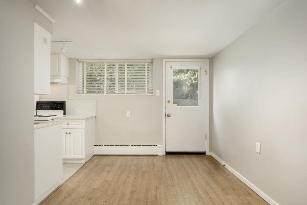 Empty kitchen in a Vancouver first-floor apartment with white cabinets, light wood-look flooring, and a glass-paneled door.