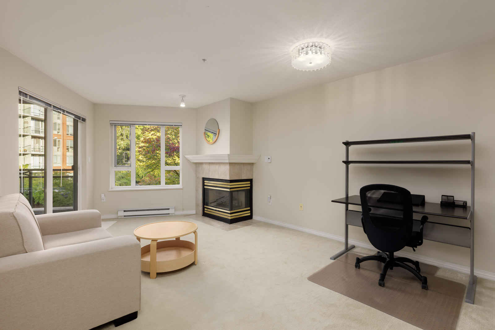 Living room at 5683 Hampton Pl. featuring a beige sofa, round wooden coffee table, fireplace, and black desk with chair.