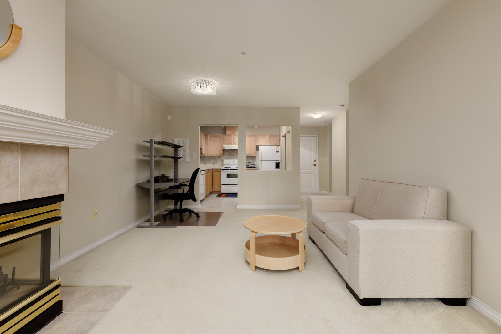 Living room at 5683 Hampton Pl with a fireplace, couch, coffee table, desk, and an open view into the kitchen.