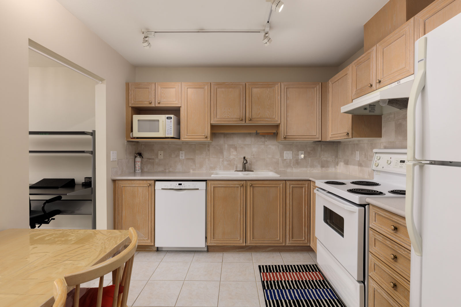 Kitchen at 5683 Hampton Pl featuring light wood cabinets, white appliances, a tiled backsplash, and a striped floor mat.