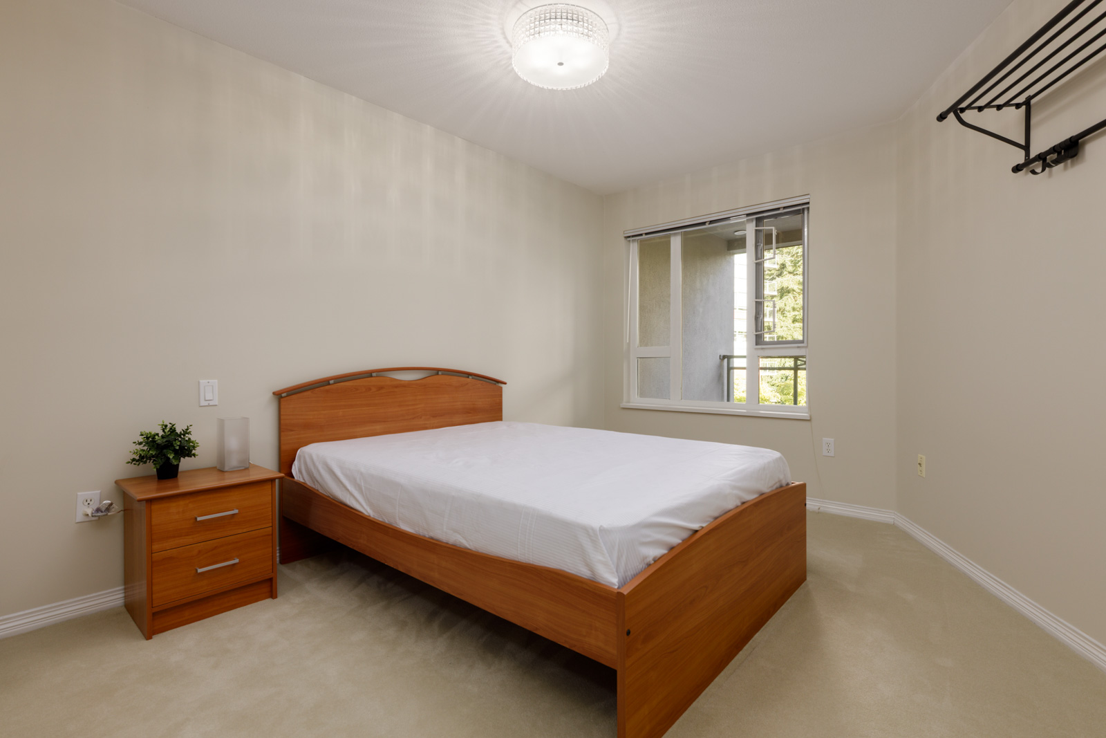 Bedroom at 5683 Hampton Pl with a wooden bed frame, a matching nightstand with a small plant, and a balcony window.