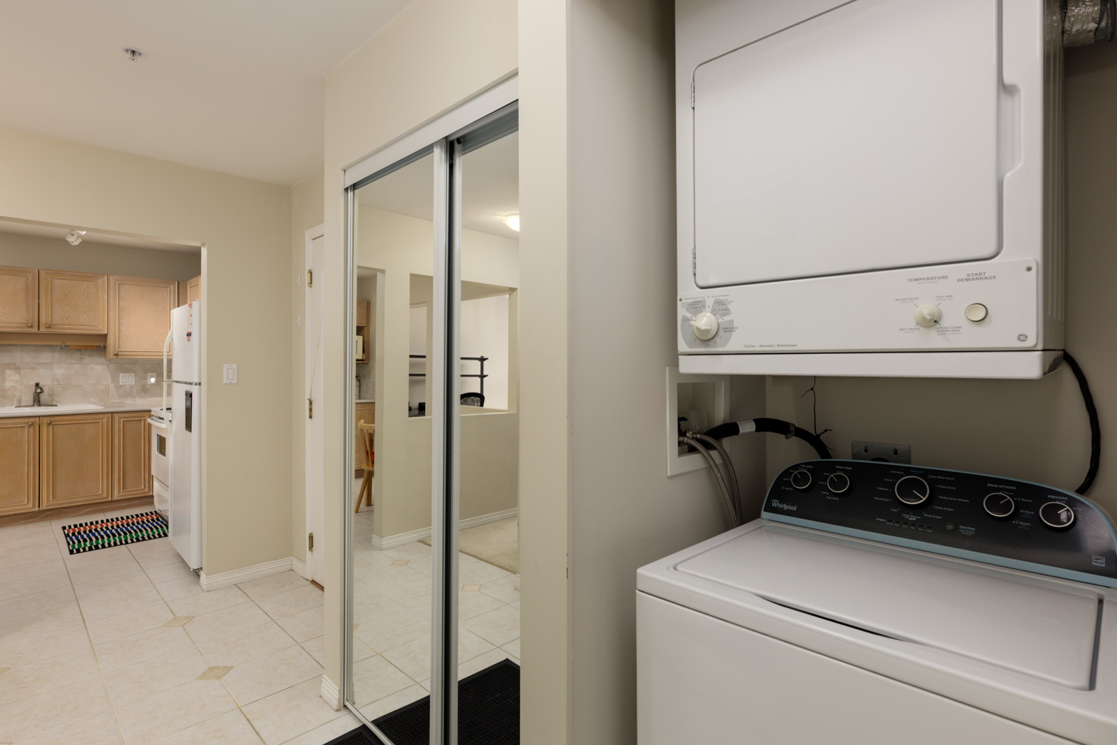 Stacked washer and dryer in a Vancouver condo hallway, beside a mirrored closet and view of the kitchen.