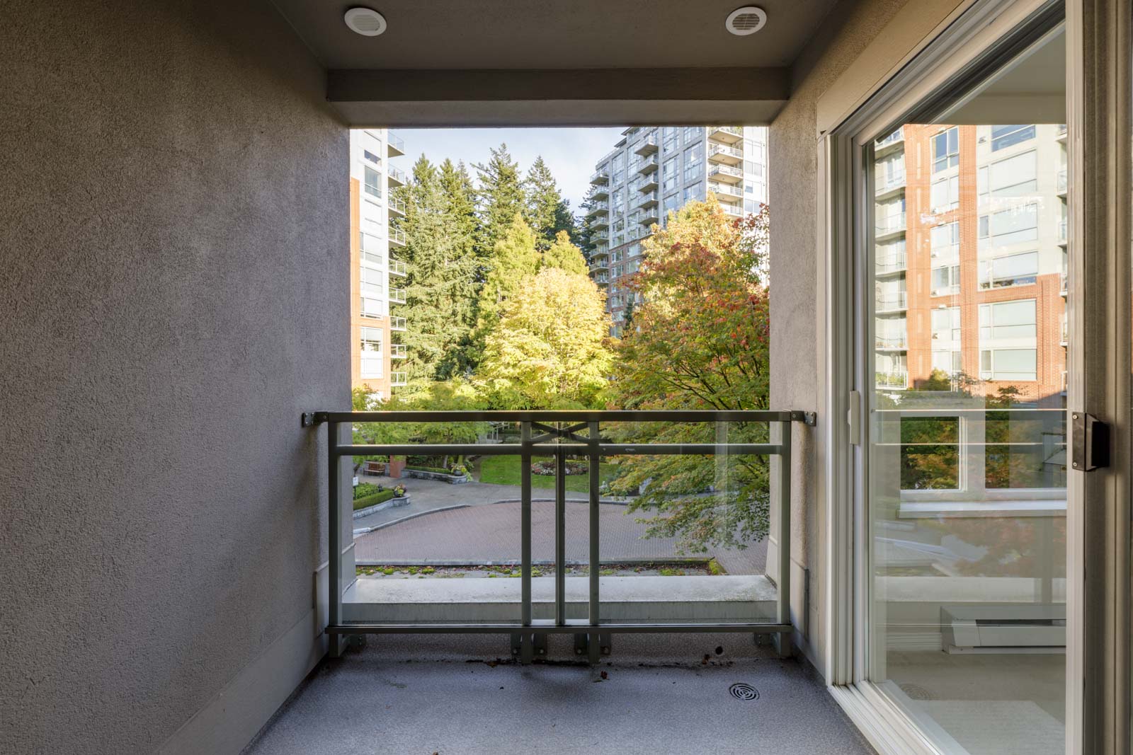 View from a covered balcony at 5683 Hampton Pl, overlooking a courtyard with trees and an apartment building.