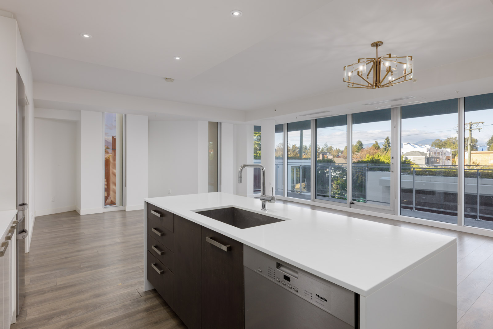 Modern kitchen at 5699 Baillie St, Vancouver, with a white island, dark cabinets, a dishwasher, and glass balcony doors.