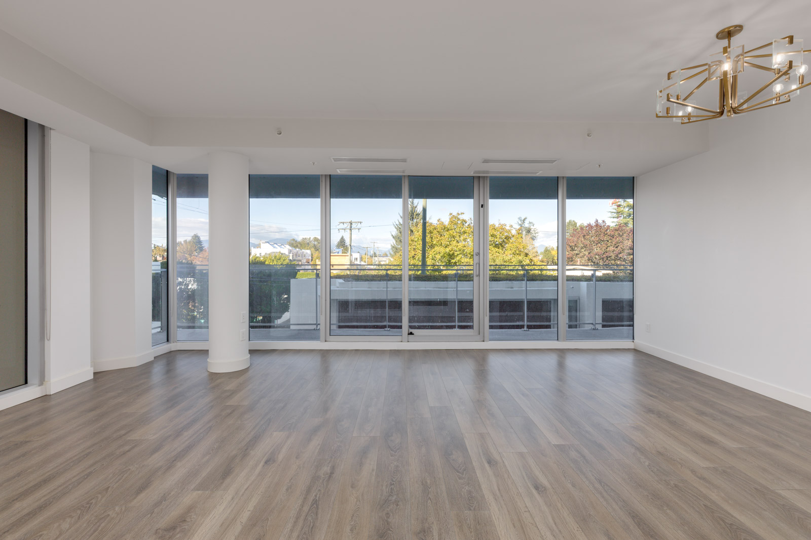 Empty room at 5699 Baillie St, Vancouver, with light wood floors, floor-to-ceiling windows, and a gold chandelier.
