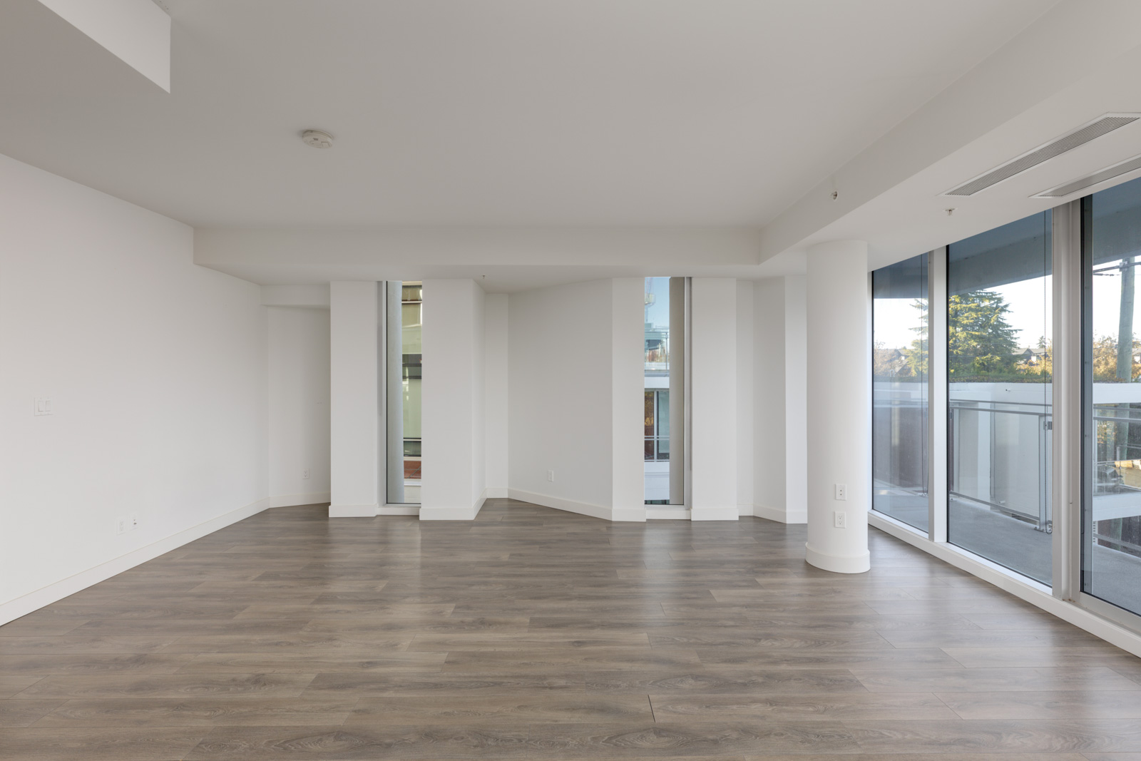 Empty Vancouver office with wood-look flooring, white walls, and floor-to-ceiling windows opening to a balcony.