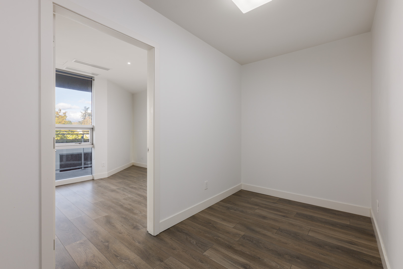 Empty room at 5699 Baillie St with white walls, wood-look flooring, and a doorway to a sunlit balcony.
