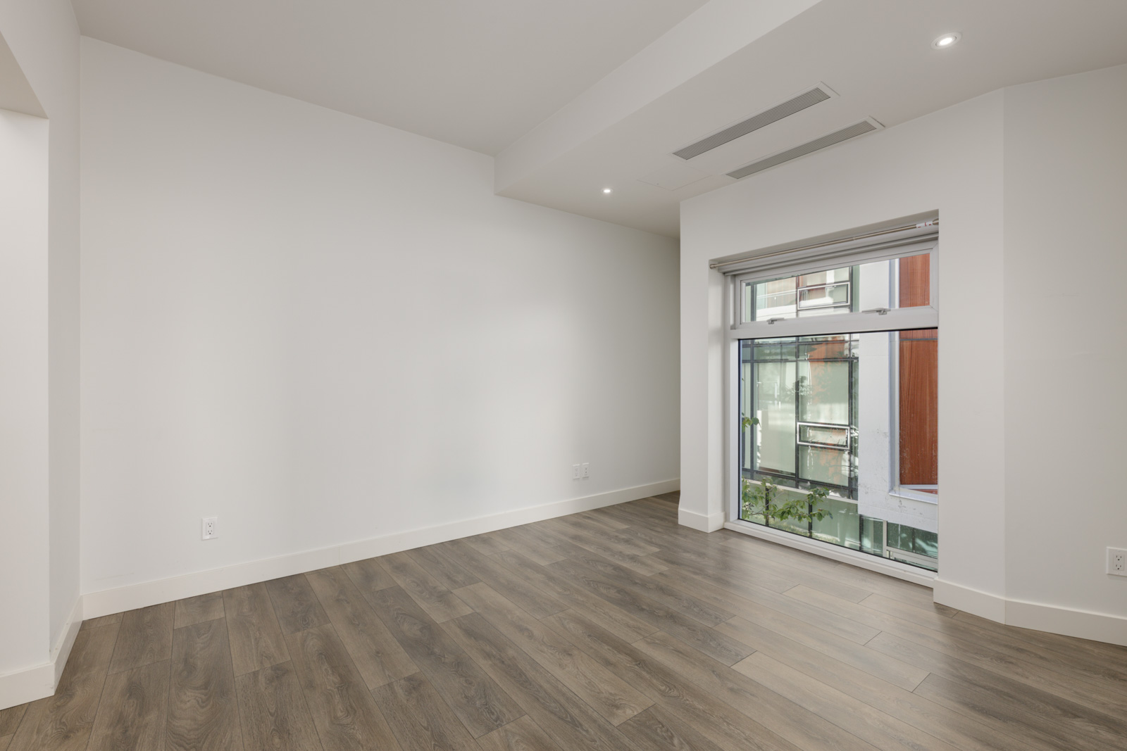 Empty room at 5699 Baillie St featuring white walls, wood-look flooring, and a large window facing a building exterior.