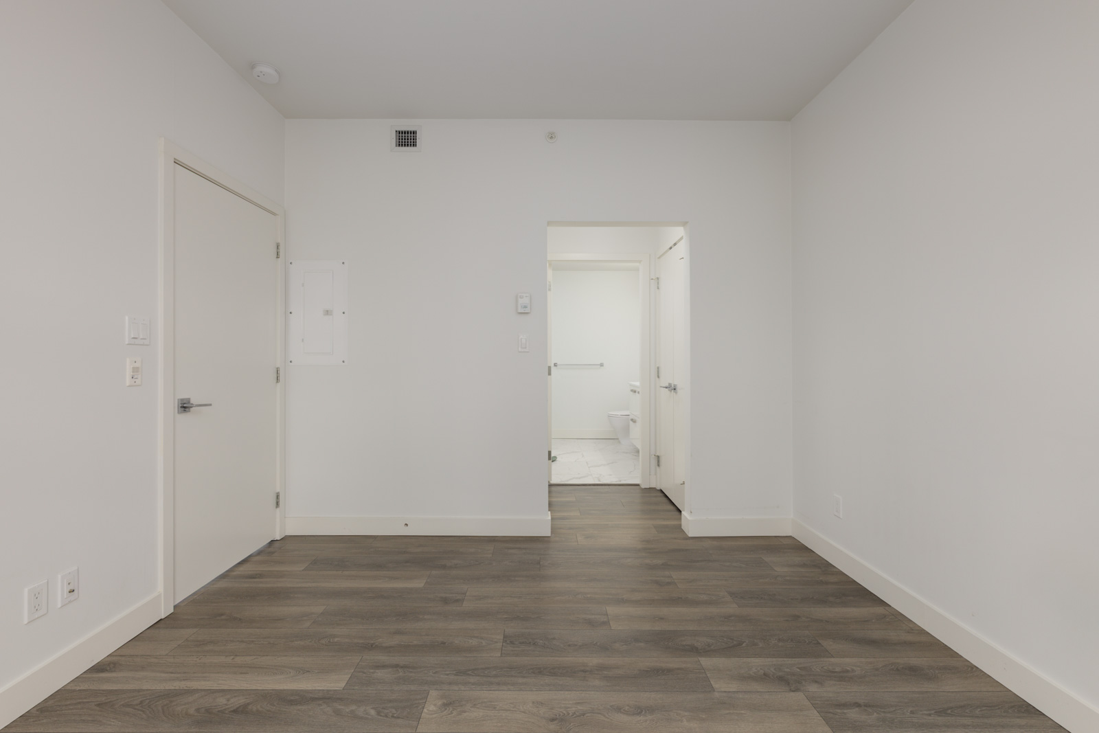 Empty white room with dark wood-look flooring and an open doorway to a bathroom at 5699 Baillie St.