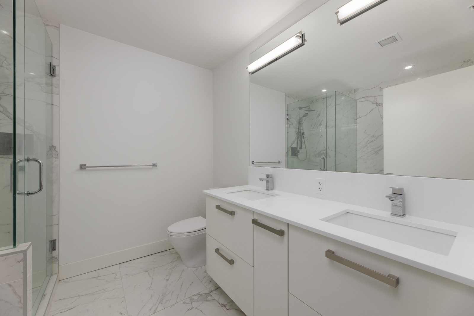 Modern bathroom at 5699 Baillie St with a double vanity, large mirror, toilet, and a glass-enclosed marble-look shower.