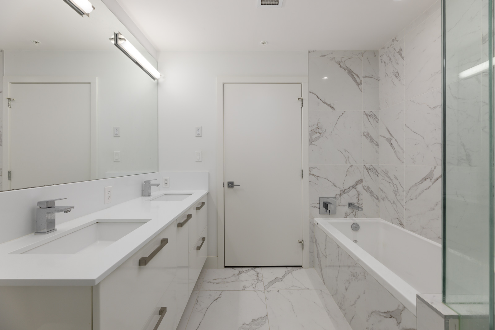 Modern bathroom at 5699 Baillie St with a white double vanity, central door, and a marble-tiled bathtub area.
