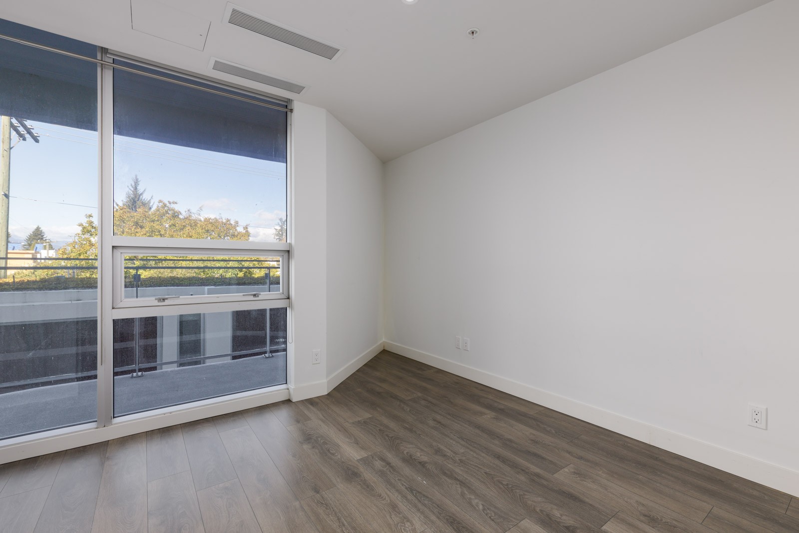 Empty corner room at 5699 Baillie St with white walls, wood-look flooring, and a large window facing a balcony.