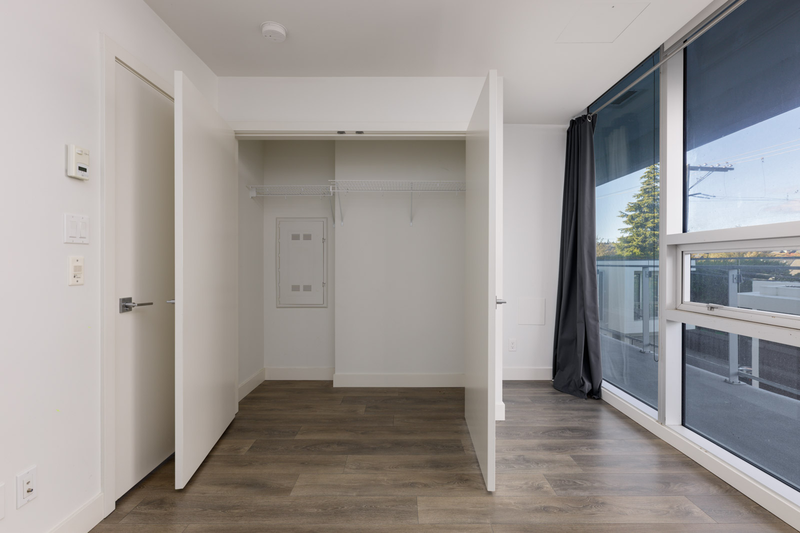 Open closet with wire shelving beside a window with grey curtains and wood-look flooring in a Vancouver home.