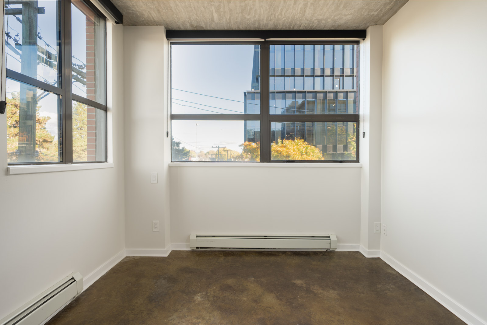 Empty room with white walls, a concrete floor, and large windows overlooking a Vancouver office street.
