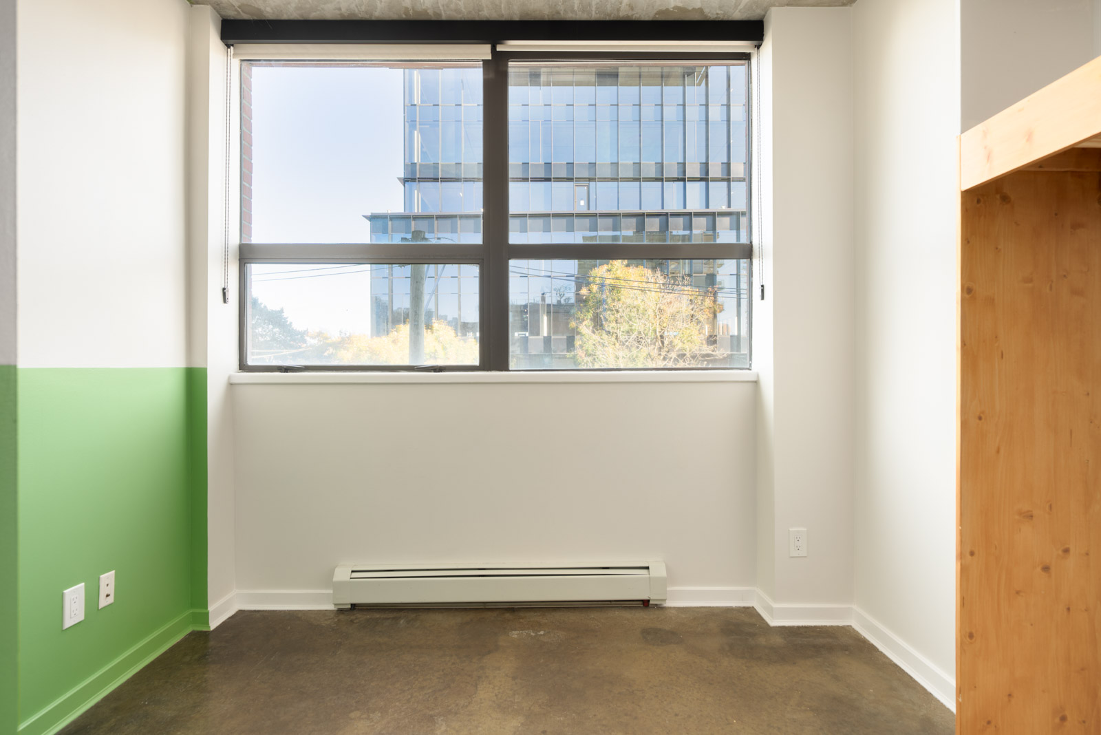 Empty office with a green accent wall and concrete floors, overlooking a building at 919 Station Street, Vancouver.