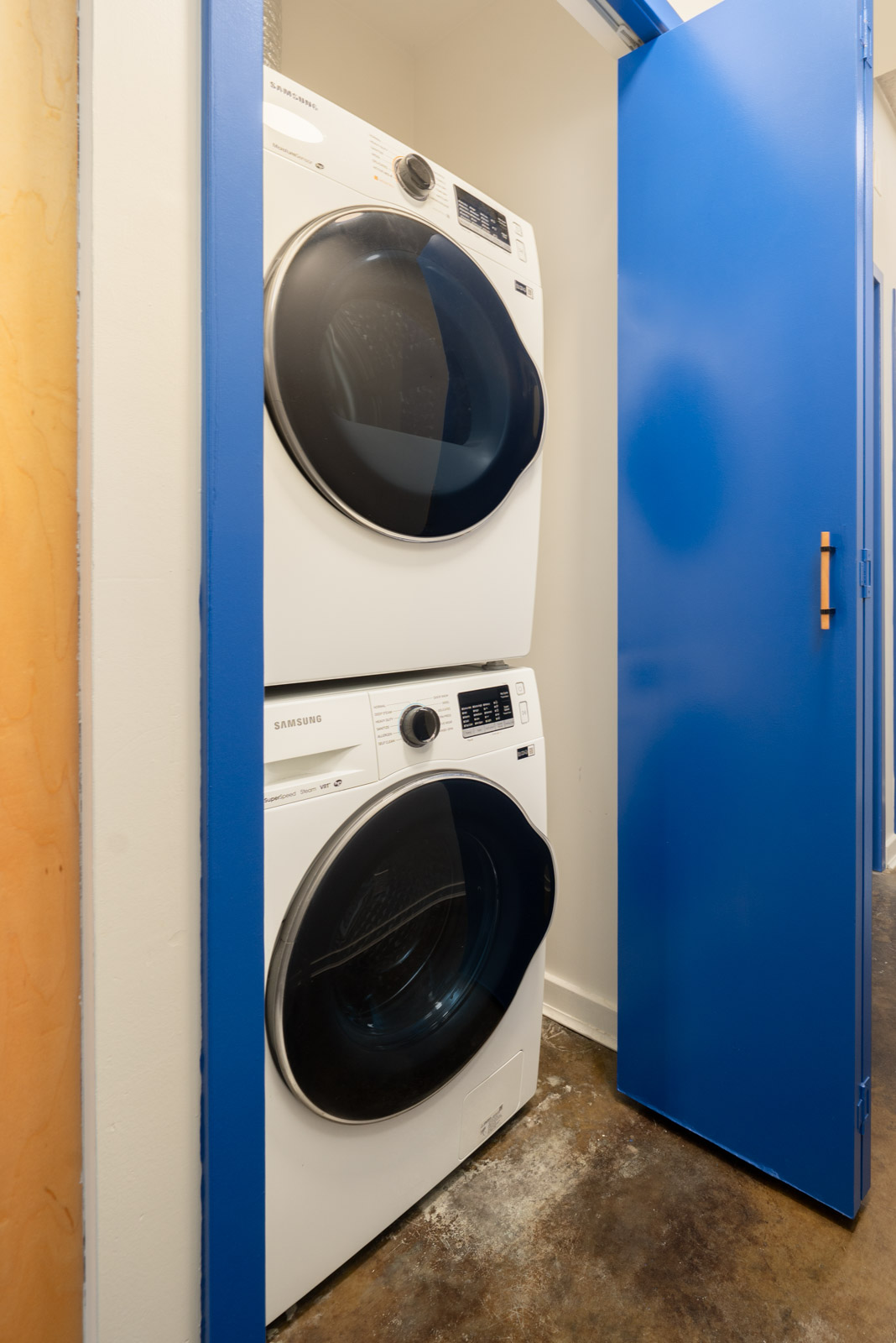 Stackable white Samsung washer and dryer in a 4th-floor Vancouver office closet with a blue door.