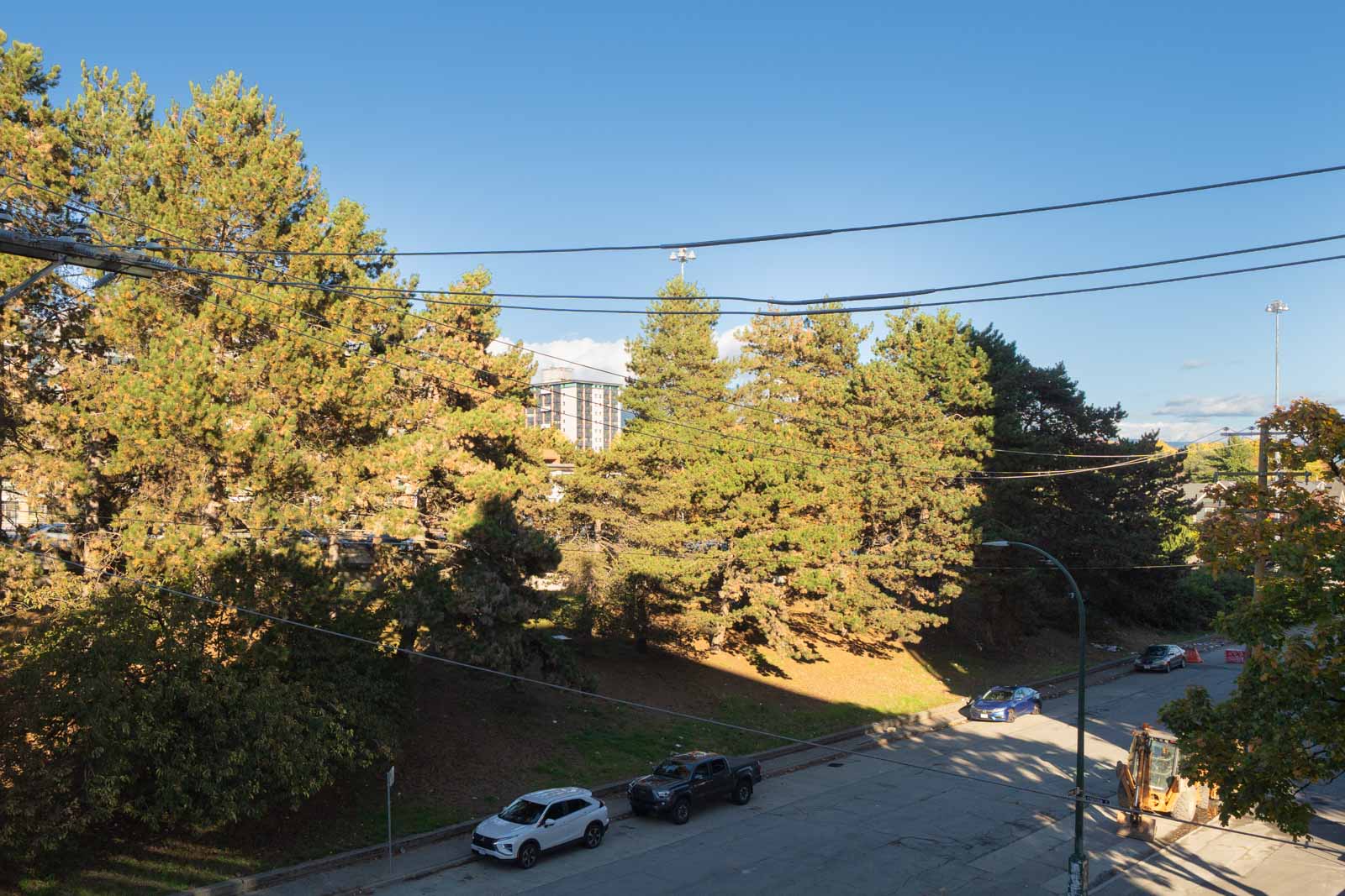 View of a tree-lined street with parked cars and a construction vehicle from a 4th-floor office at 919 Station St, Vancouver.