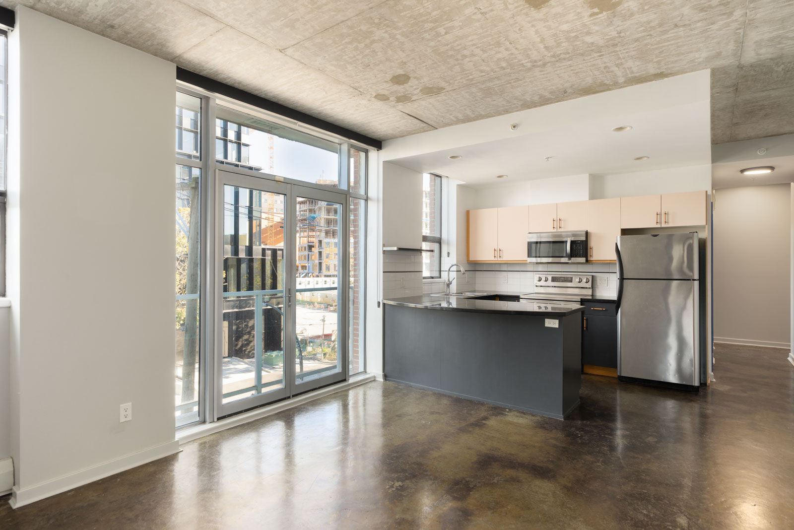 Modern kitchen at 919 Station Street with concrete ceilings, dark cabinetry, and glass doors opening to a balcony.