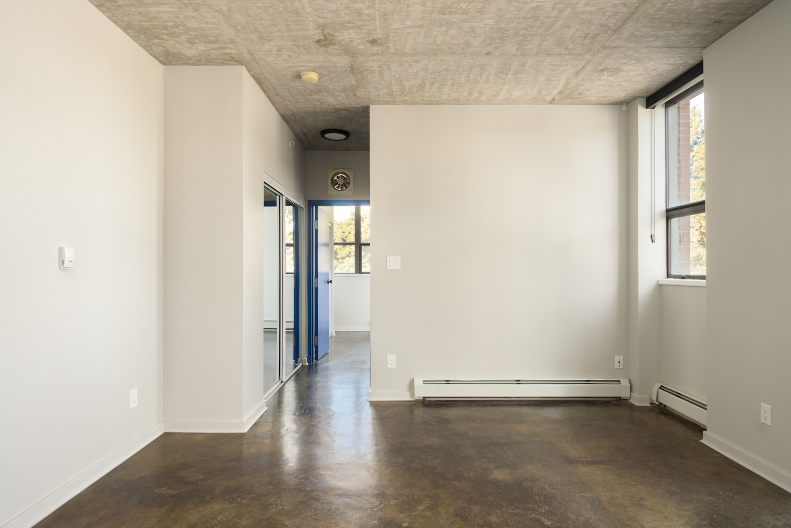 Empty apartment at 919 Station Street featuring concrete ceilings, polished floors, and a blue door to a hallway.
