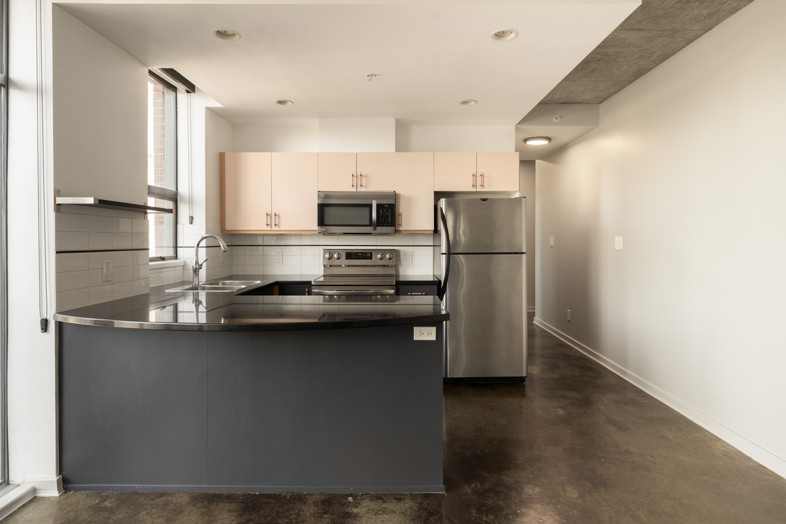 Modern kitchen at 919 Station Street featuring a dark curved island, stainless steel appliances, light cabinets, and concrete floors.