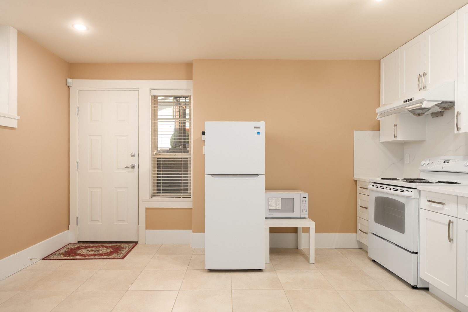 White appliances—refrigerator, microwave, and stove—in a Yew St kitchen with tan walls and tiled floors.
