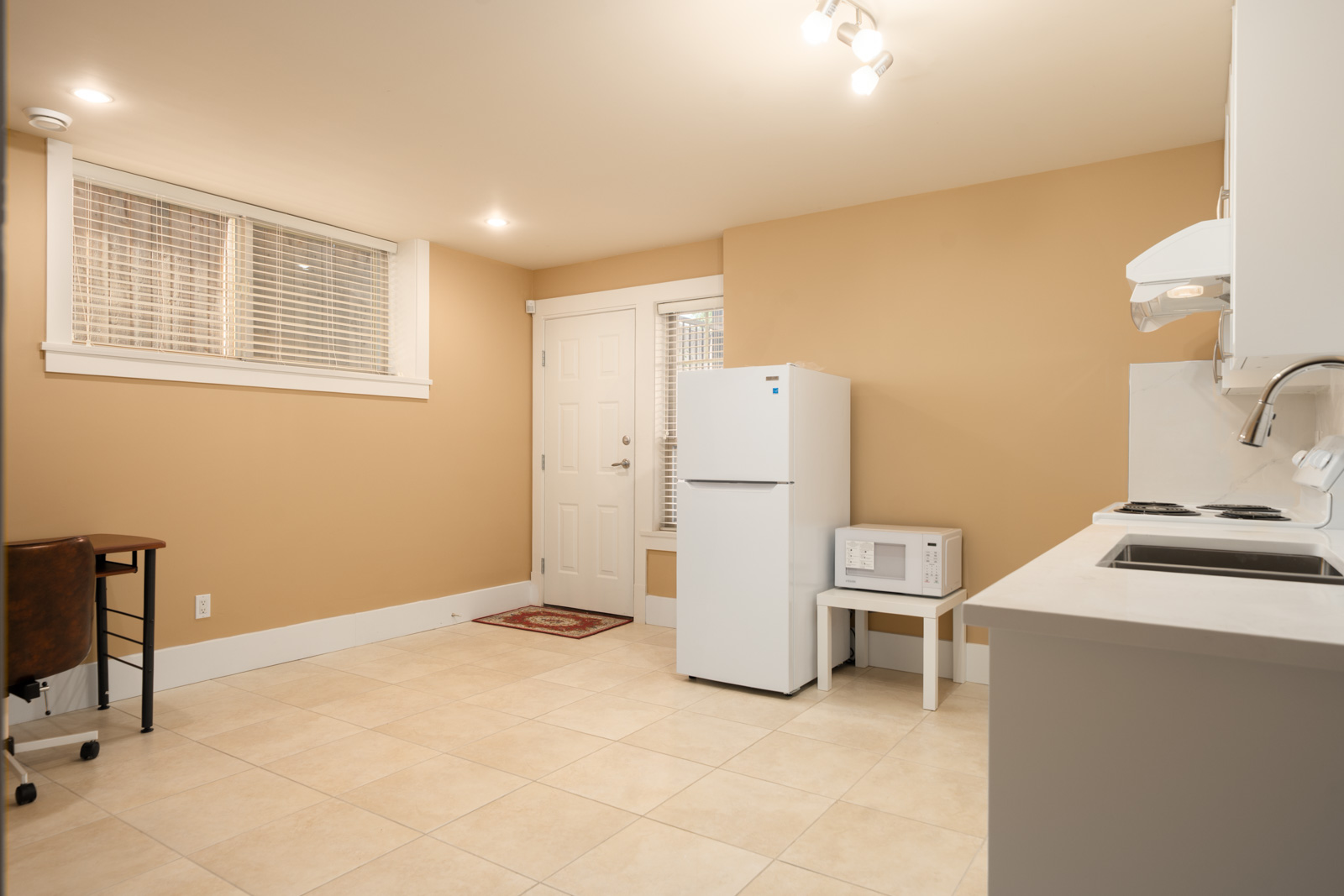 Kitchen in a Yew St basement featuring a small white refrigerator, a microwave on a stool, and a corner desk.