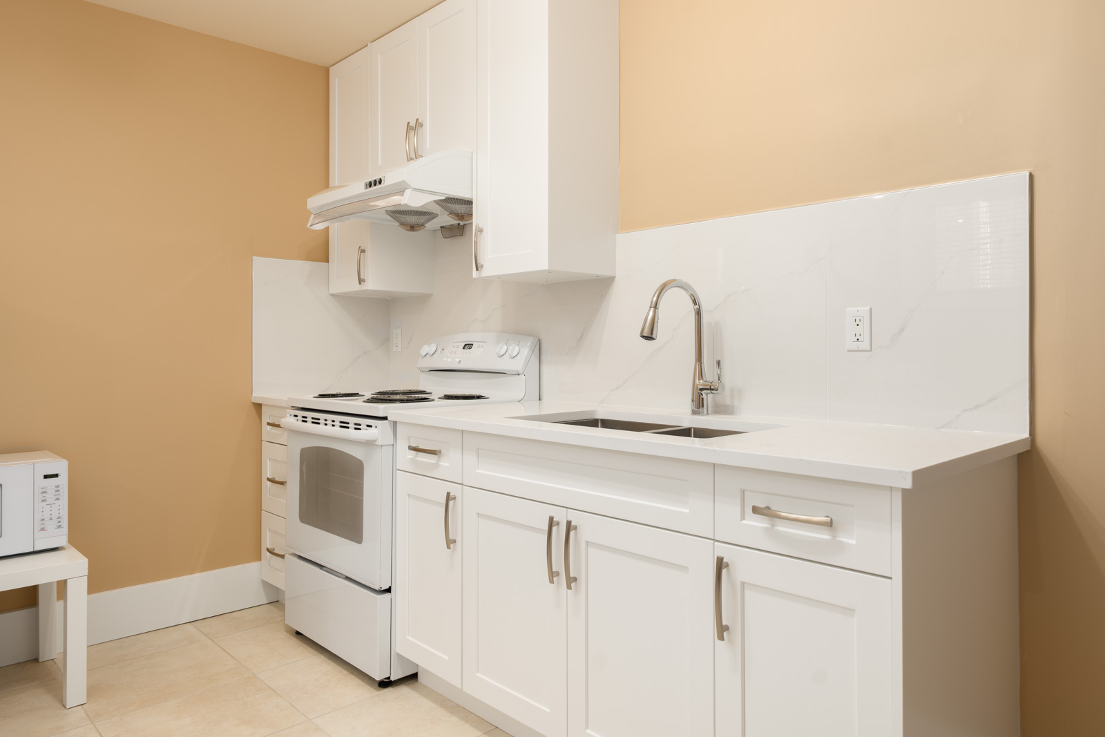White kitchen featuring a range, hood, sink, and cabinets against tan walls in a West 22nd Ave home.