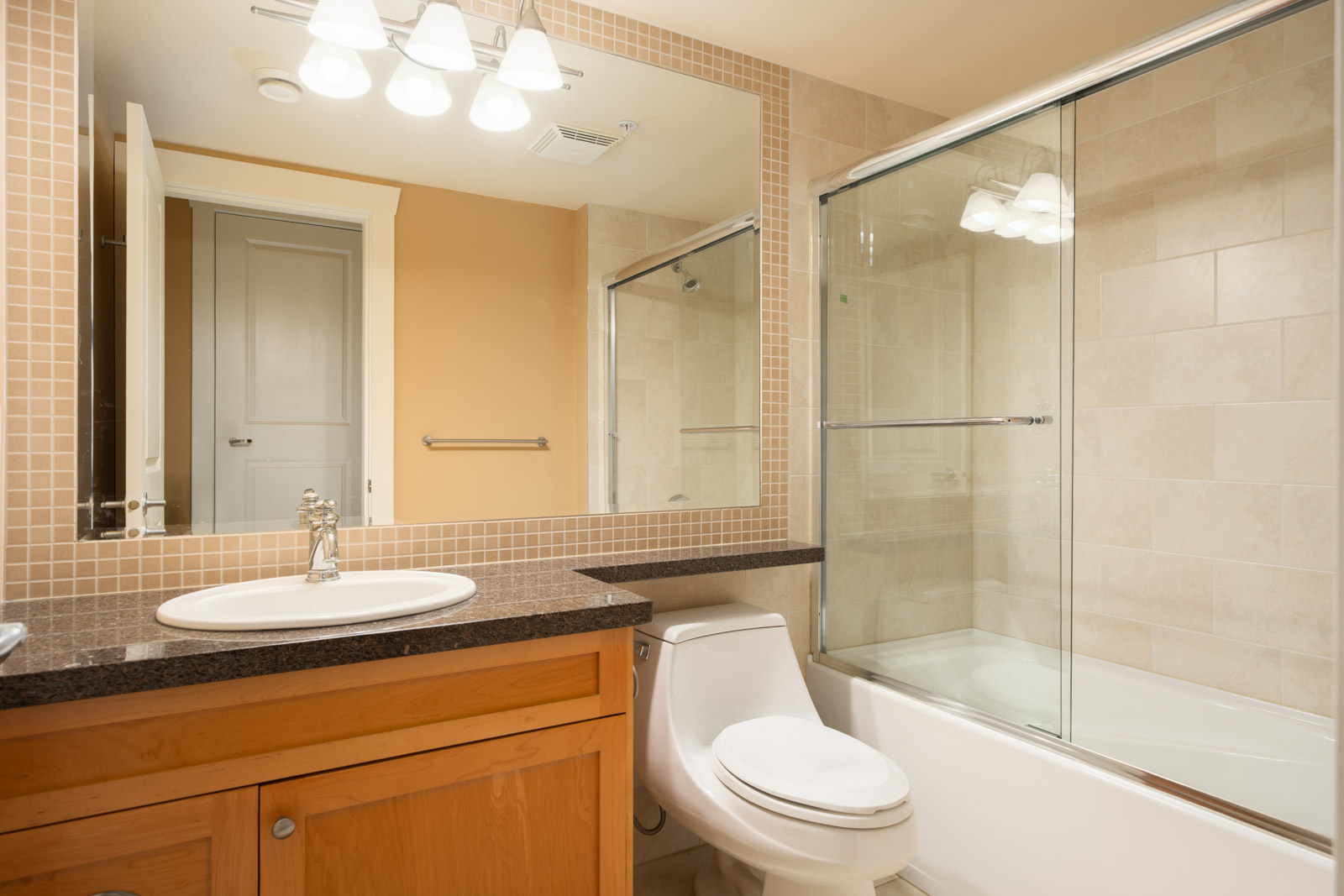 Bathroom at the West 22nd Ave residence with a vanity sink, toilet, and a glass-enclosed shower/tub combo.
