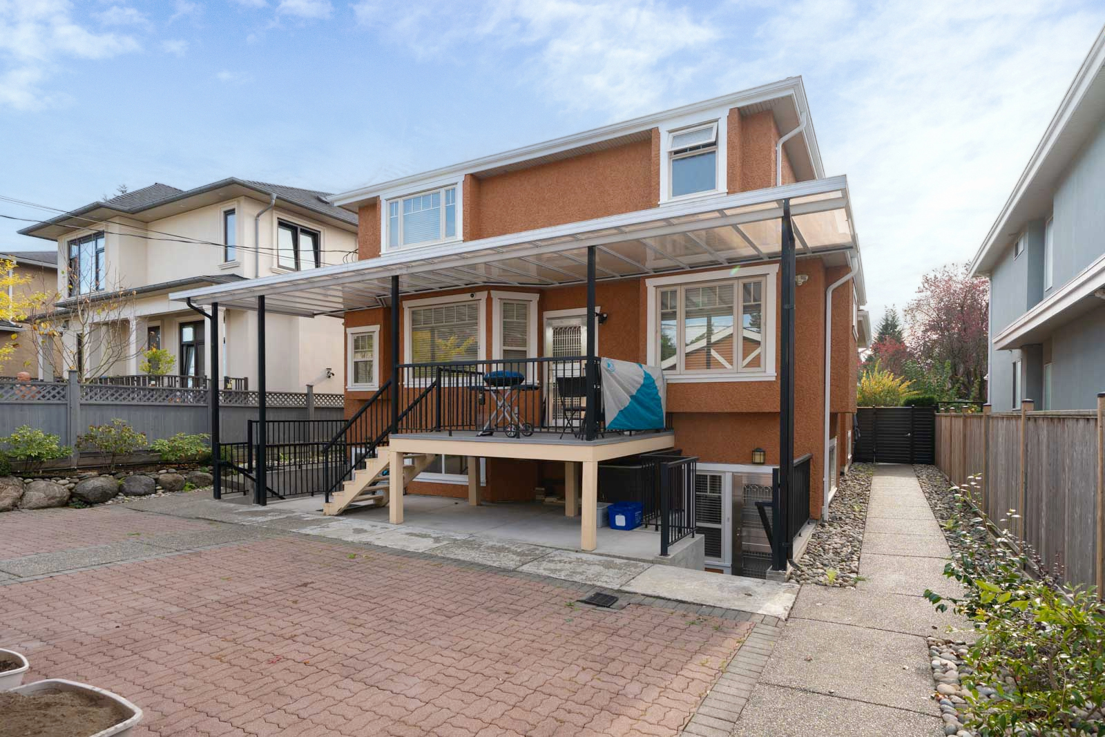 Rear view of a two-story orange house on West 22nd Ave, featuring a raised wooden deck with a transparent patio roof.